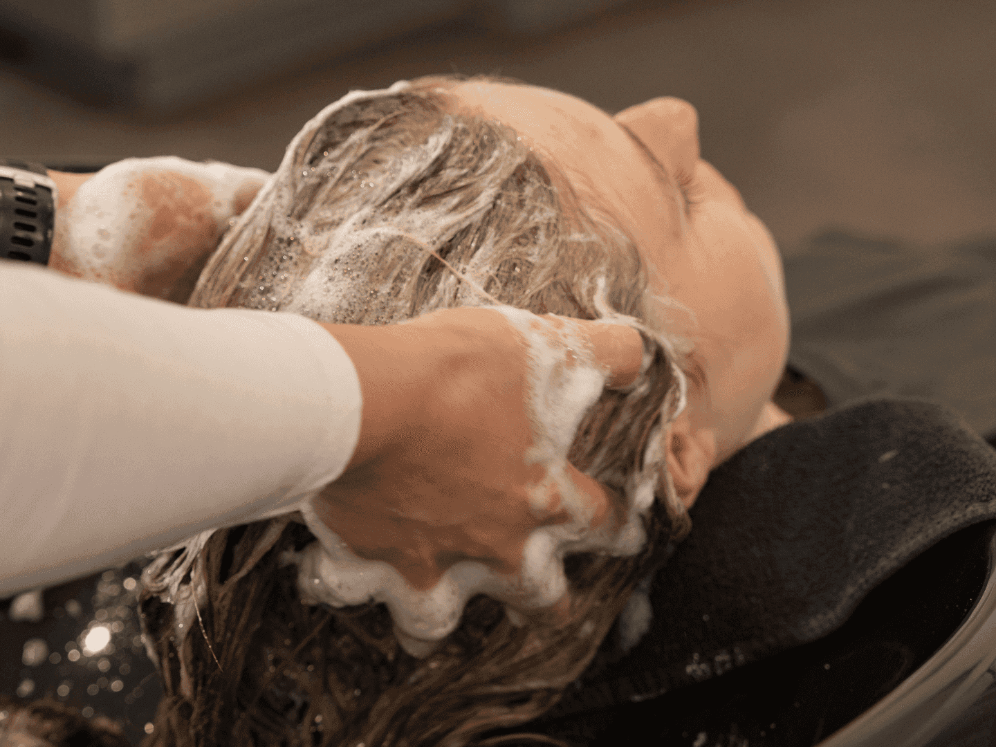 Person getting a hair wash at a salon, relaxing with foam lather in hair.