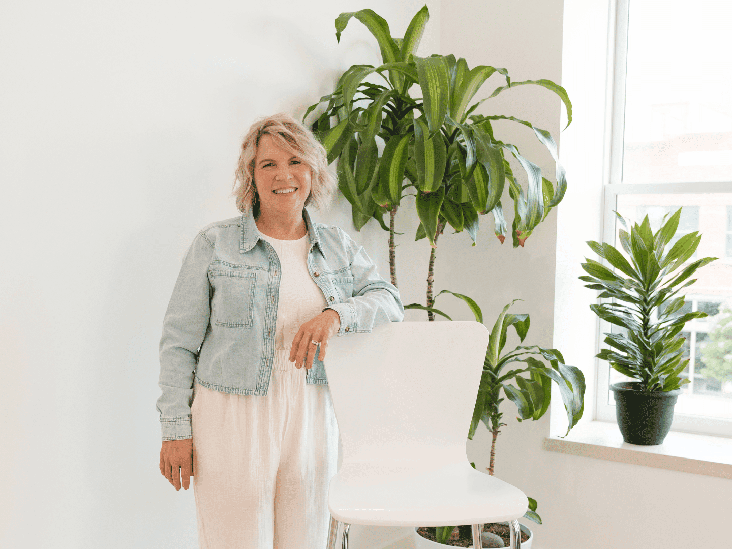 Woman smiling near potted plants in a bright, modern interior setting.