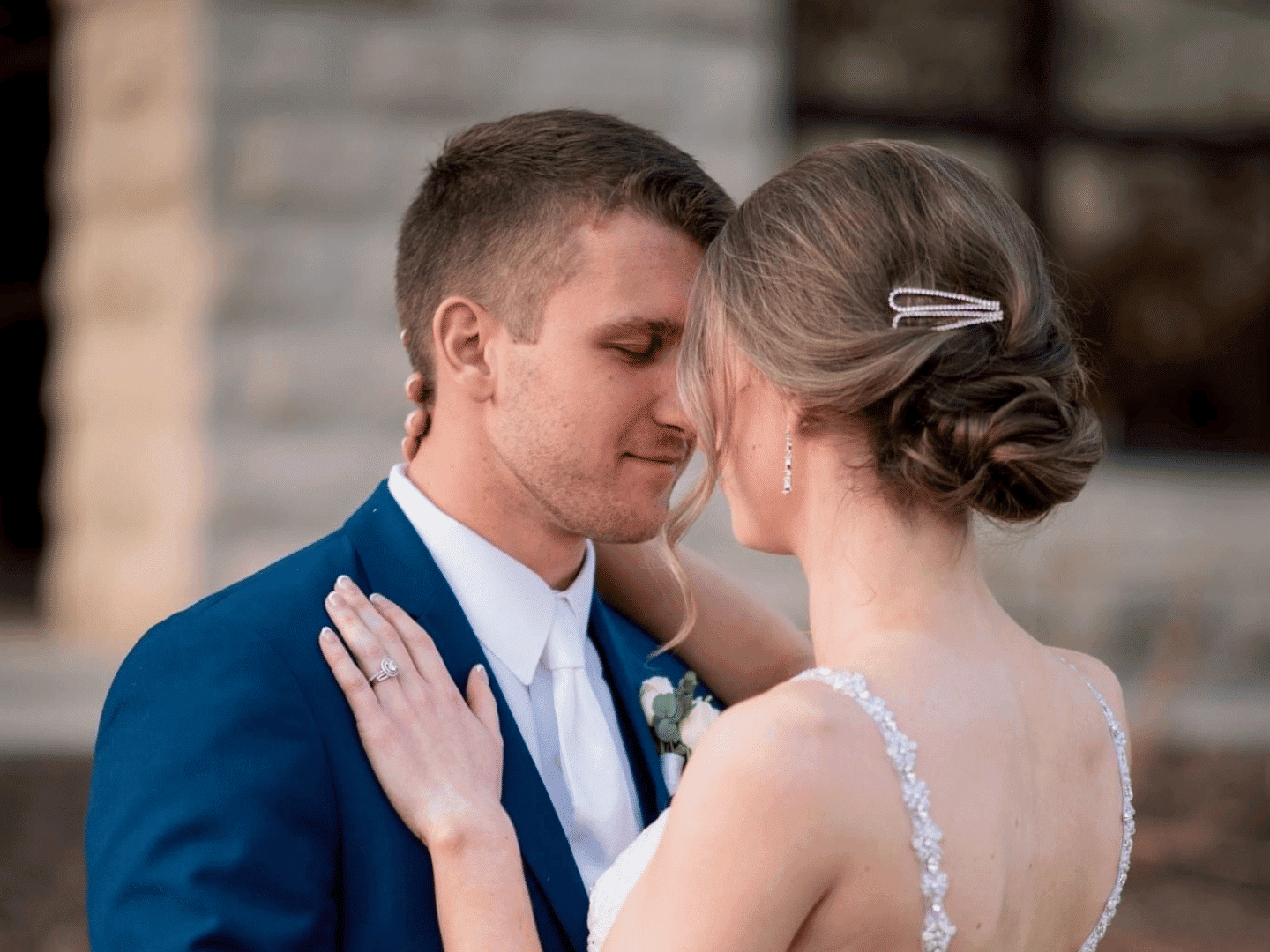 Couple embracing, dressed in formal attire with soft focus background.