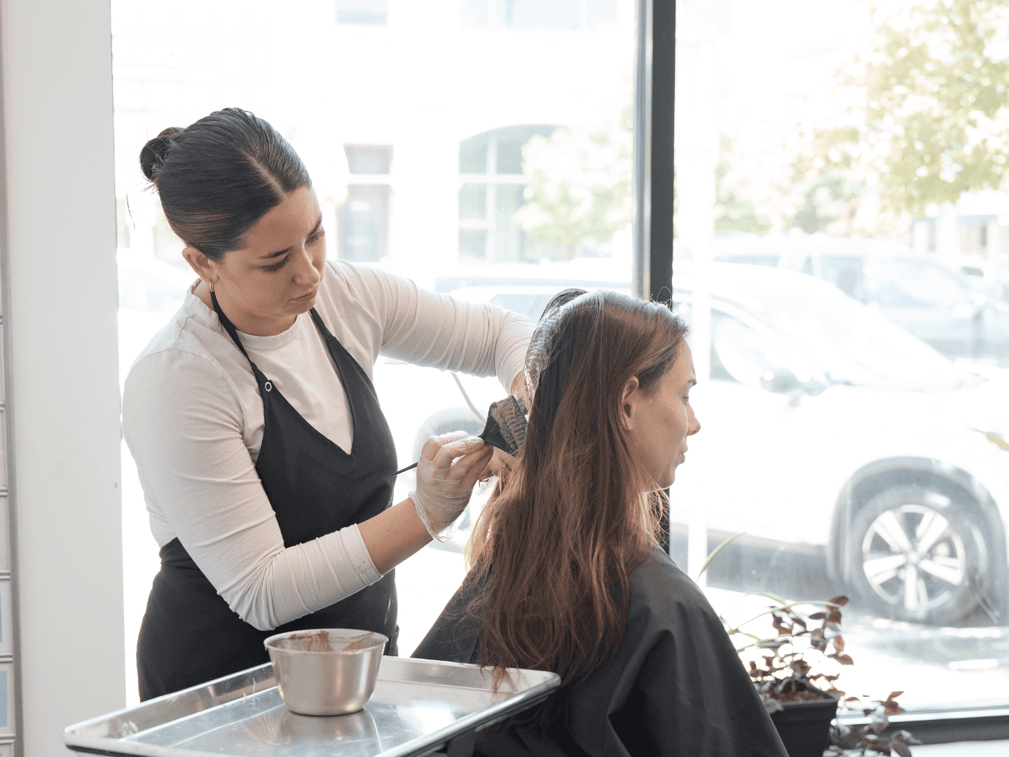 Woman in salon getting her hair dyed by a stylist wearing gloves and apron.